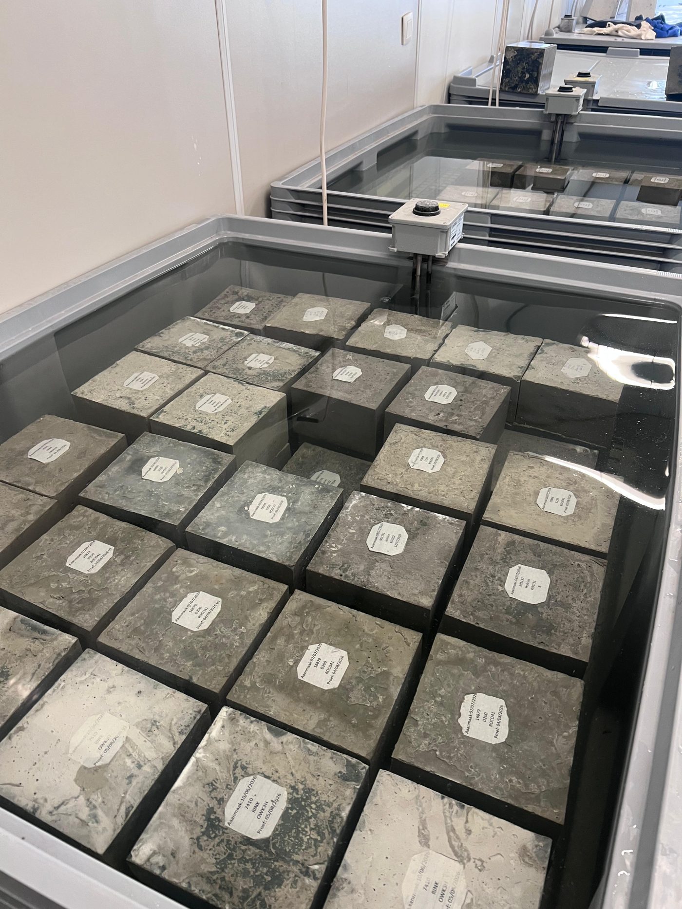 Gelabelde betonkubussen die in het labo uitharden in een waterbad