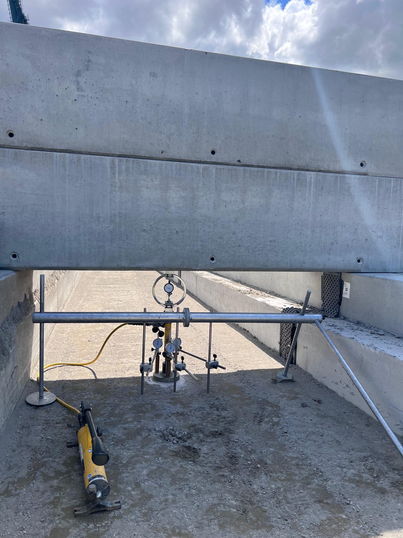 Statische plaatproef op een werf: belastingsopstelling met meetklokken en hydraulische pomp onder een betonbalk
